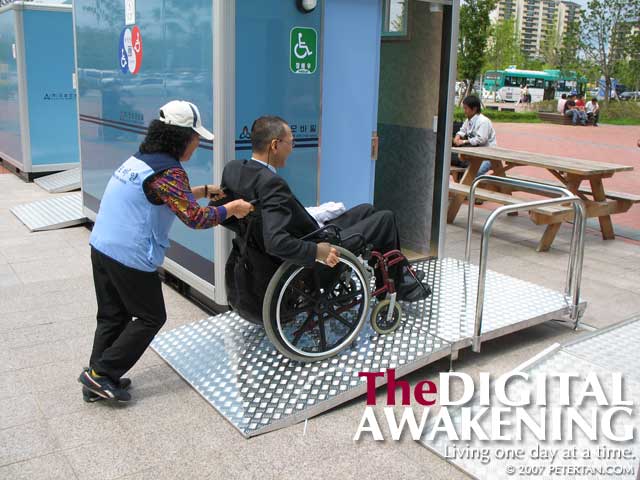 Cleaning lady assisting me into the portable accessible toilet at the 7th Disabled Peoples' International World Assembly